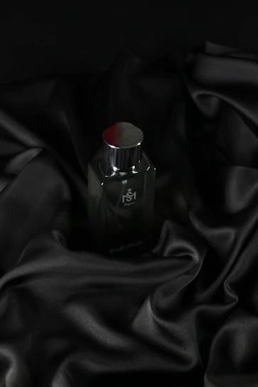 A sleek dark bottle of Nevjorx perfume with golden accents on a black marble surface.