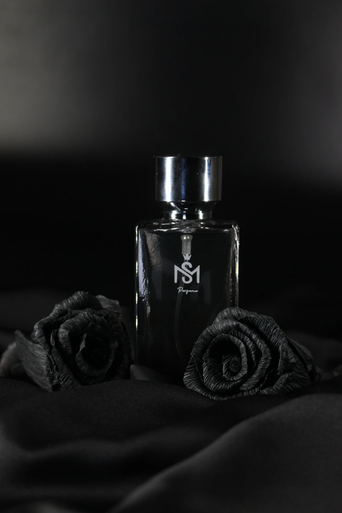 Frasco escuro e rosas negras sobre tecido preto