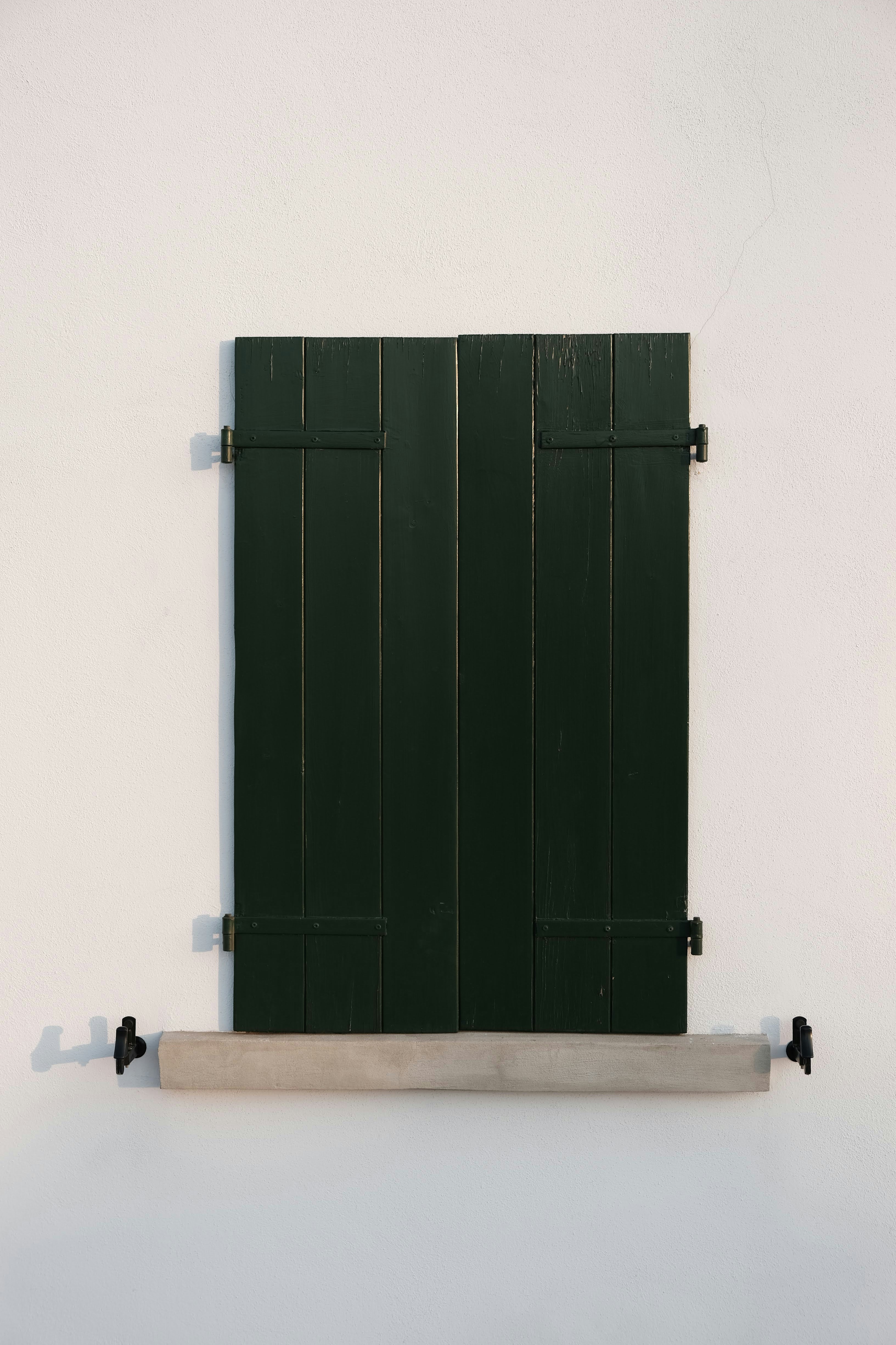 a window with green shutters on a white wall