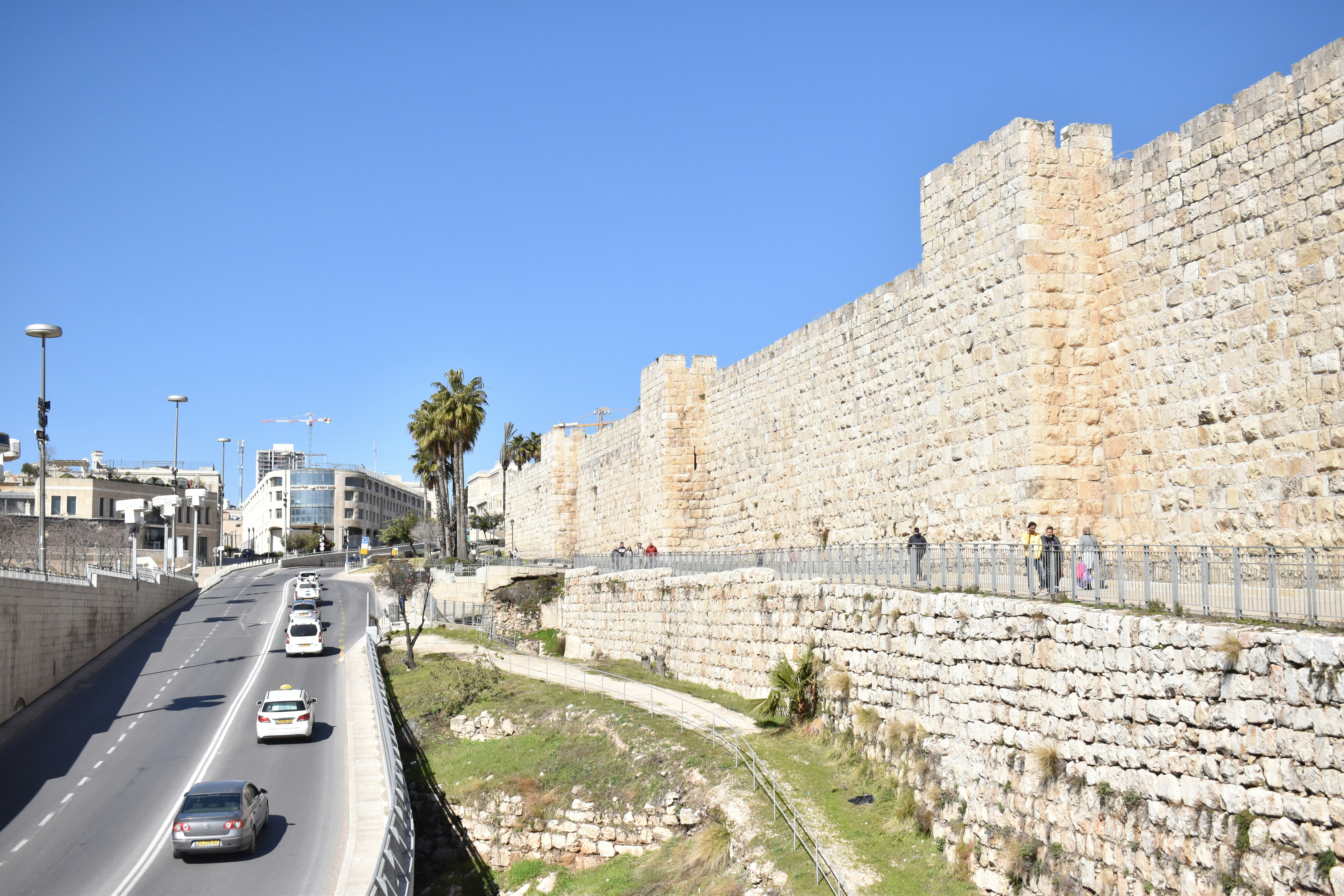 cars driving down a road next to a stone wall