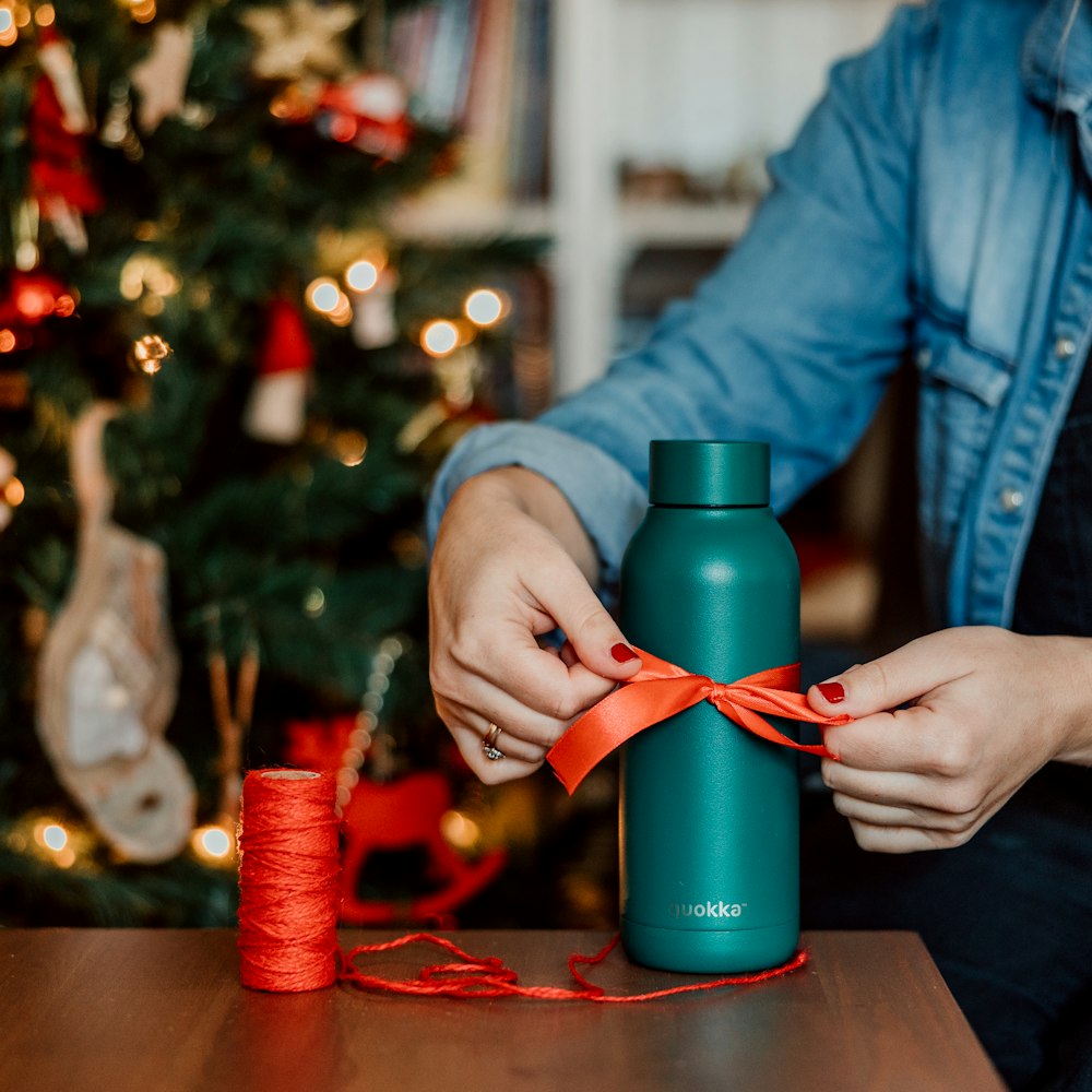 a person tying a ribbon around a green water bottle