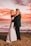 a bride and groom embracing on the beach at sunset