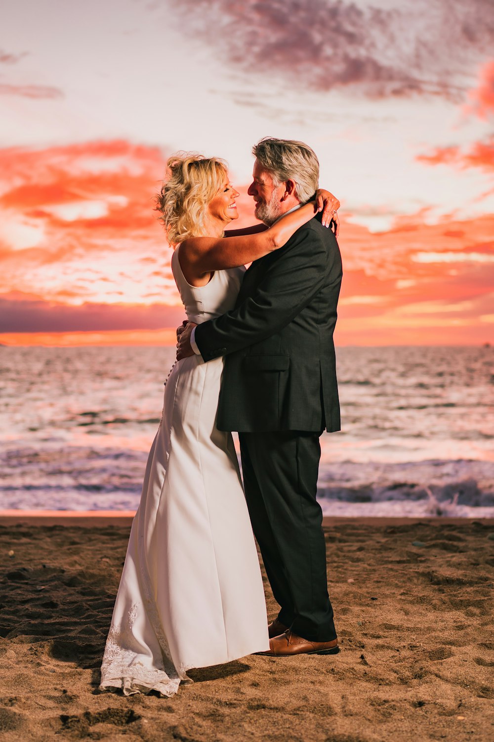 uma noiva e noivo abraçados na praia ao pôr do sol