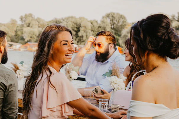 A lively group of people sharing laughs around a beautifully decorated outdoor event table at sunset.