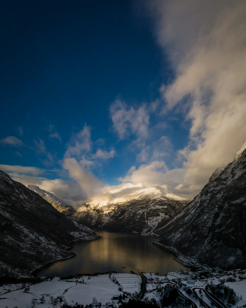 a lake surrounded by snow covered mountains under a cloudy sky