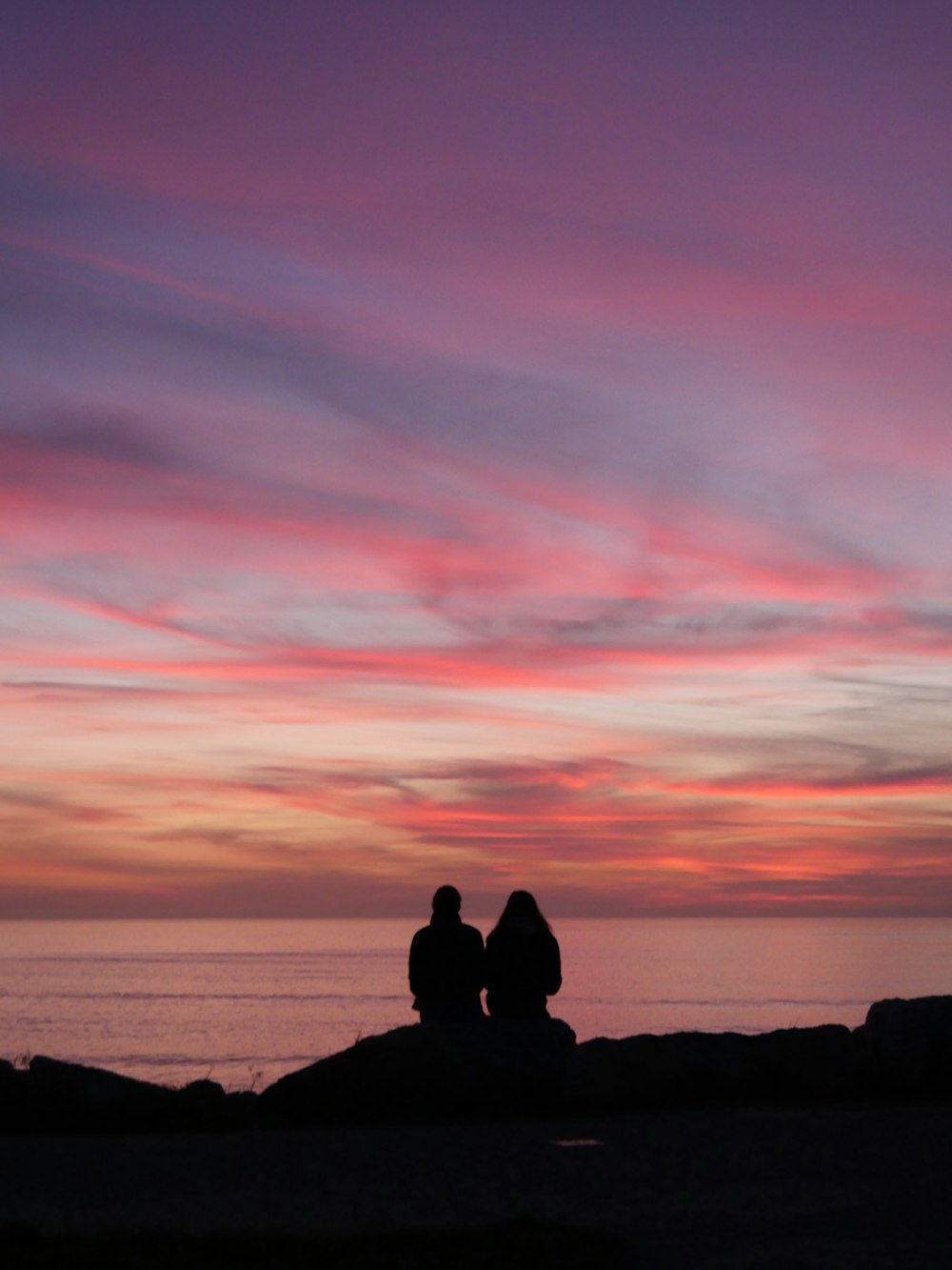 two people sitting on a rock watching the sunset