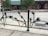 A decorative metal fence features silhouettes of hands reaching outwards in various directions. Behind the fence, there is a street scene with trees, a bicycle, and shops including one with a green and white striped awning labeled 'Hill Market'. The environment is urban and appears calm.
