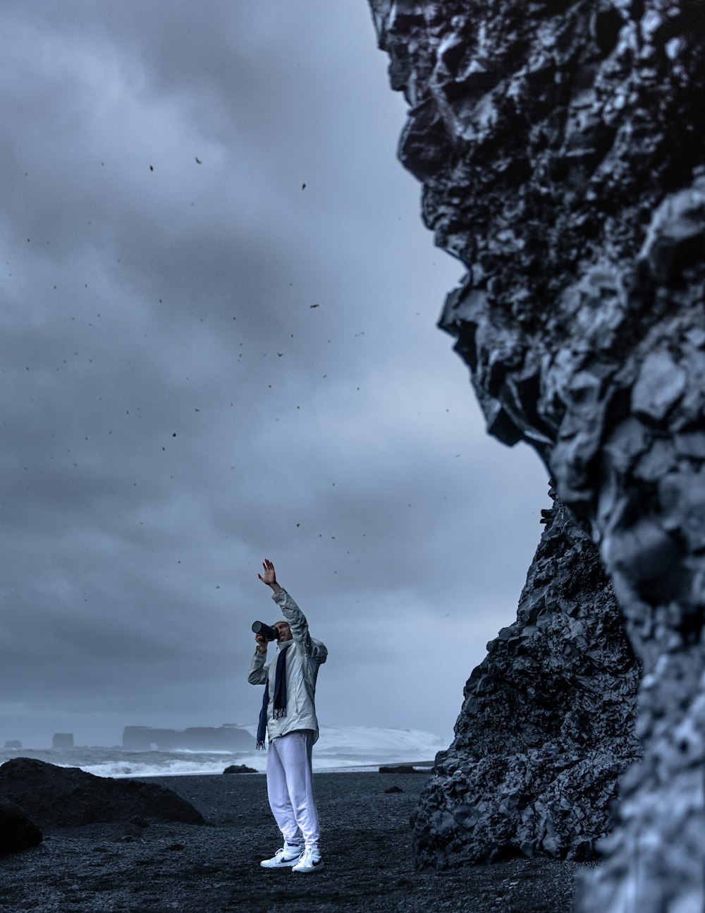 a man standing on top of a rocky beach under a cloudy sky