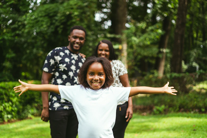 a little girl with her arms outstretched in front of two adults