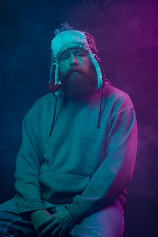 a man with a beard wearing a hat and smoking a cigarette
