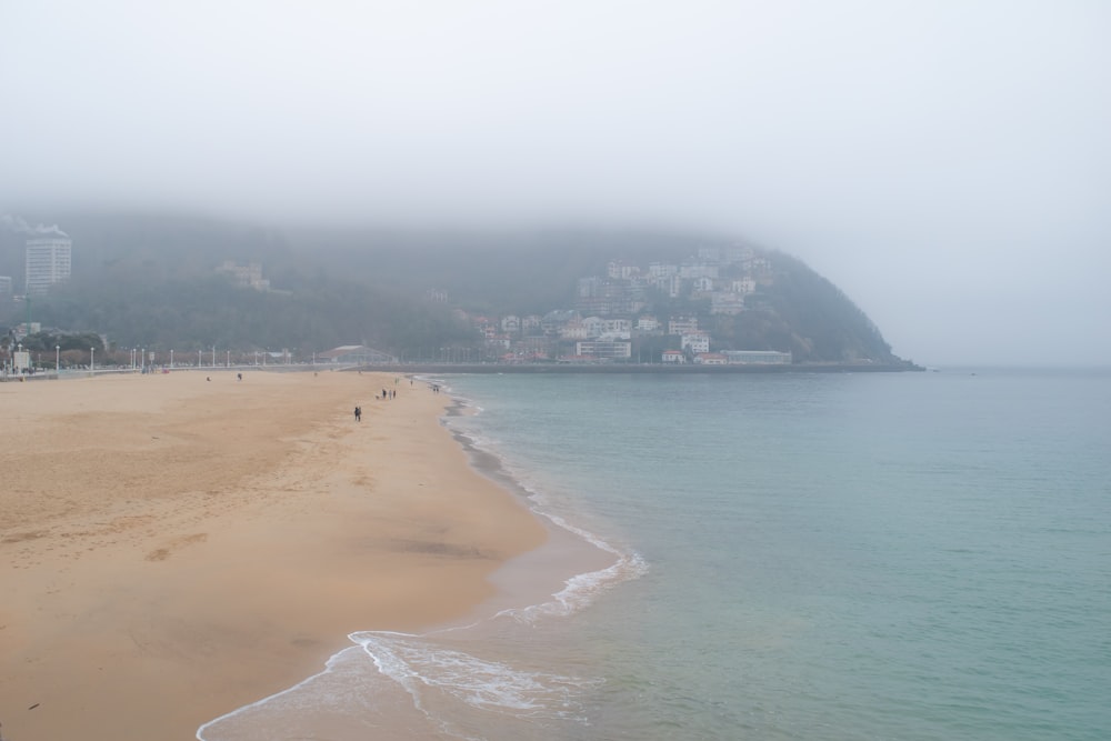 a foggy day at a beach with people walking on the sand