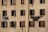 A beige apartment building facade with several windows that have dark brown shutters. Some windows are open, and there are various pieces of clothing and laundry hanging on clotheslines strung between the windows.