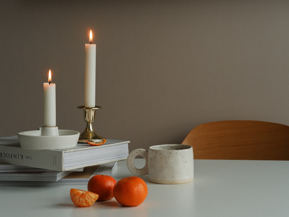 a white table topped with two white candles and two oranges
