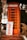 An orange telephone booth is situated on a brick sidewalk. In front of it, there is a sign that reads 'Come in we are open' with bold orange letters. The area around the booth features some greenery and outdoor elements.