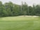 A lush golf course with a well-maintained green and sand bunkers. Surrounding the course are dense trees and foliage.