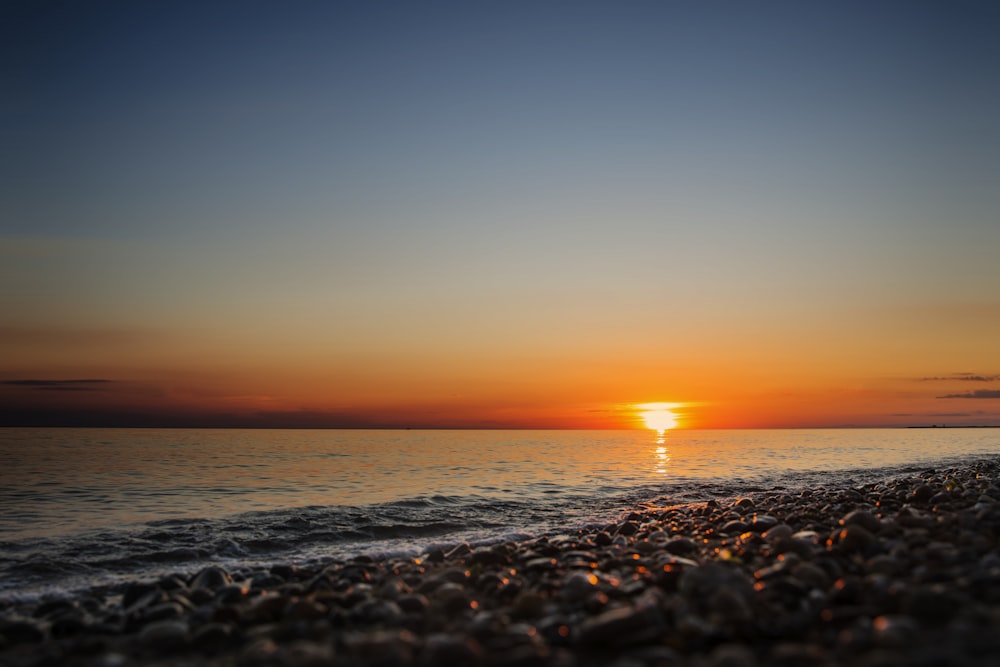 the sun is setting over the water on the beach