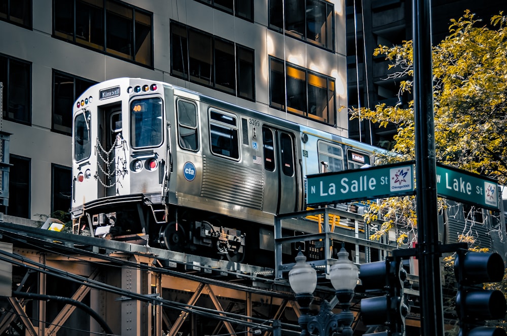 a silver train traveling down tracks next to a tall building