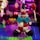 A colorful Lego clown figure is prominently displayed on a Lego baseplate. The clown is designed with a variety of bricks in bright colors like red, blue, yellow, and black. It features large eyes, a prominent red nose, and is holding a red lollipop-like object. The background is vibrant, filled with blurred lights and colors, creating a festive and playful atmosphere.