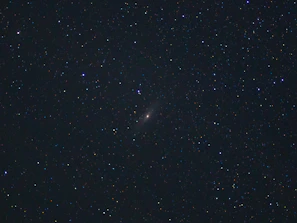 A starry night sky with a glowing quasar shining in the distance.