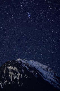 the night sky with stars above a mountain
