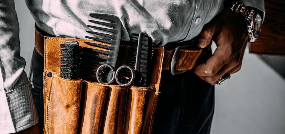 a man is holding a leather belt with combs and scissors in it