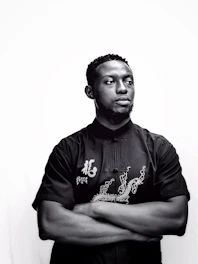 A stylish man wearing a premium black t-shirt with a subtle embroidered logo, standing against a clean white background.