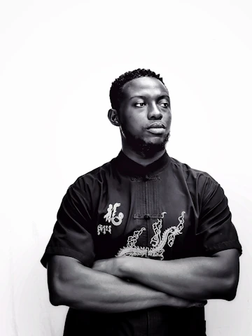 A stylish man wearing a premium black t-shirt with a subtle embroidered logo, standing against a clean white background.