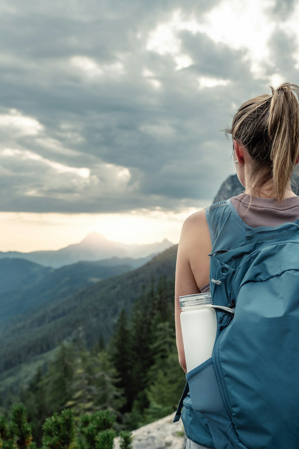 a woman with a backpack and a cup of coffee looking at the mountains