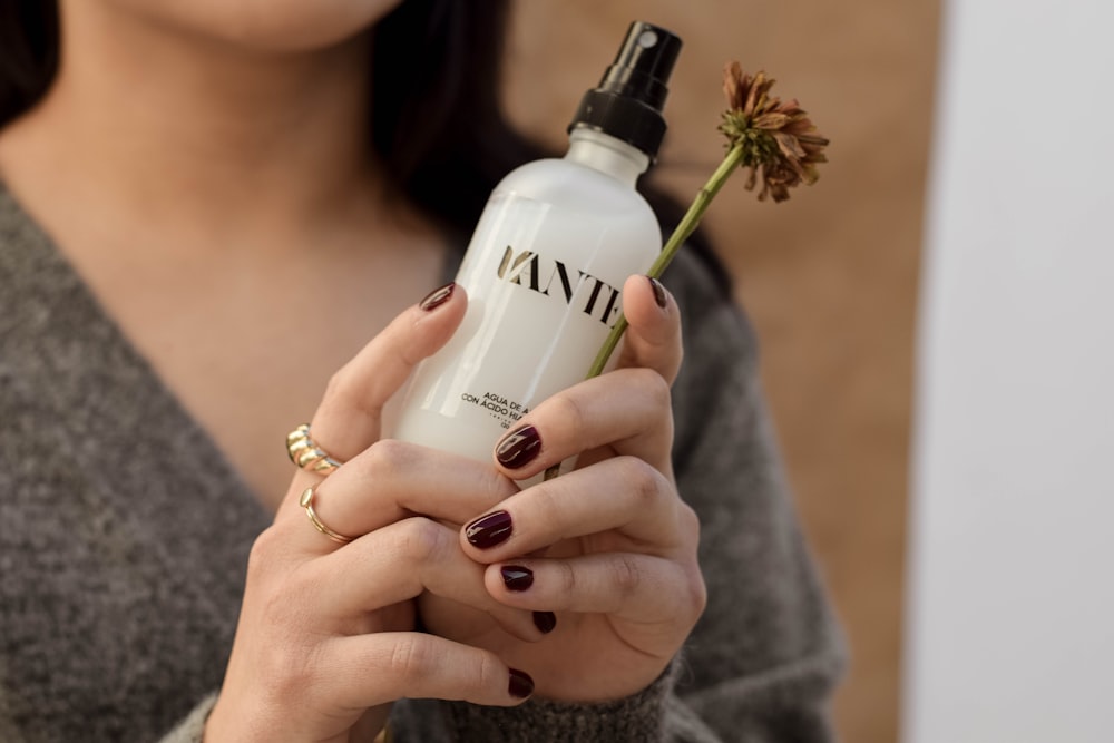 a woman holding a bottle of tanning lotion and a flower