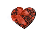 A heart-shaped gift box adorned with a large, bright red ribbon. The box is black with various red heart patterns covering its surface.