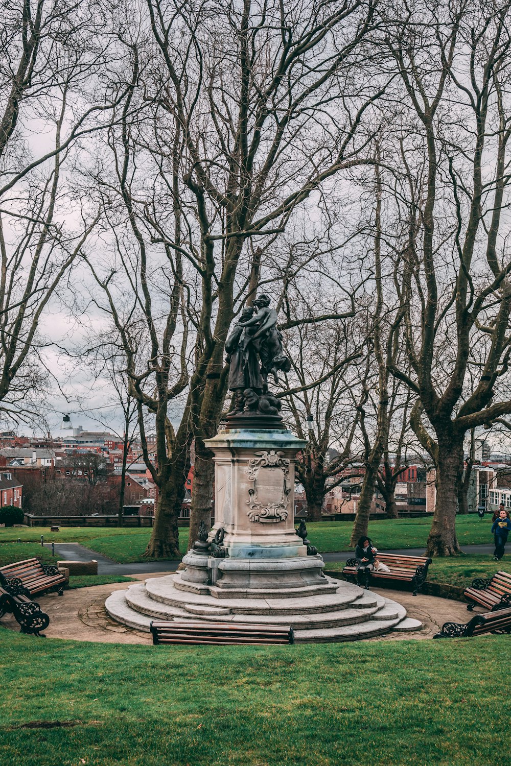 a statue in the middle of a park surrounded by trees