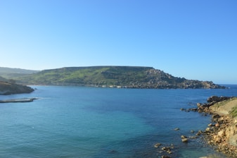 A serene Irish coastline with rolling green hills under a soft blue sky