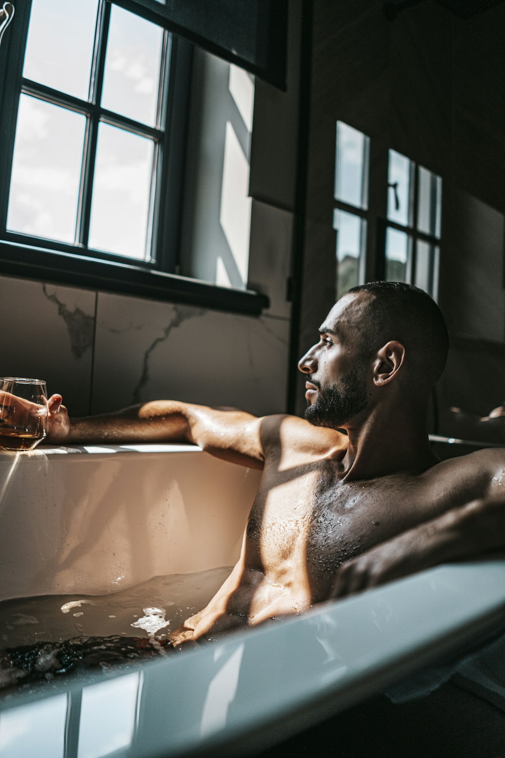 Un hombre sentado en una bañera sosteniendo una copa de vino