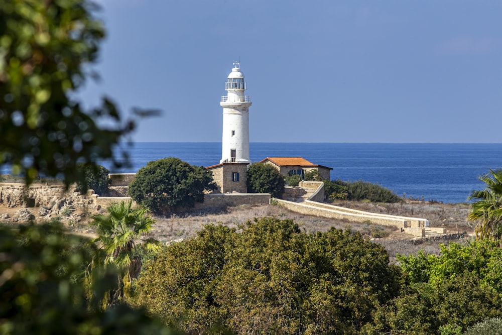 a white light house sitting on top of a hill next to the ocean