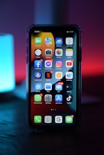 A smartphone displaying its home screen with various app icons such as Facebook, Messenger, Instagram, Netflix, and TikTok. The screen shows notifications on messaging and social media apps, indicating recent activity. The device is placed in a dark ambiance with a gradient background of blue and red tones, creating a modern and sleek appearance.