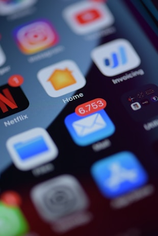 A smartphone screen displays multiple app icons, including Netflix, Instagram, Home, and Invoicing. The email app shows a notification bubble with 6,753 unread messages, and there is a red notification dot on the Netflix app.