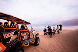 a group of people standing around a buggy in the sand