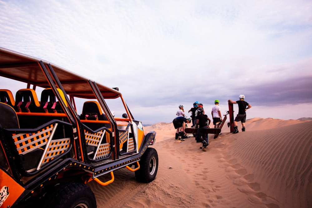 um grupo de pessoas em pé em torno de um buggy na areia