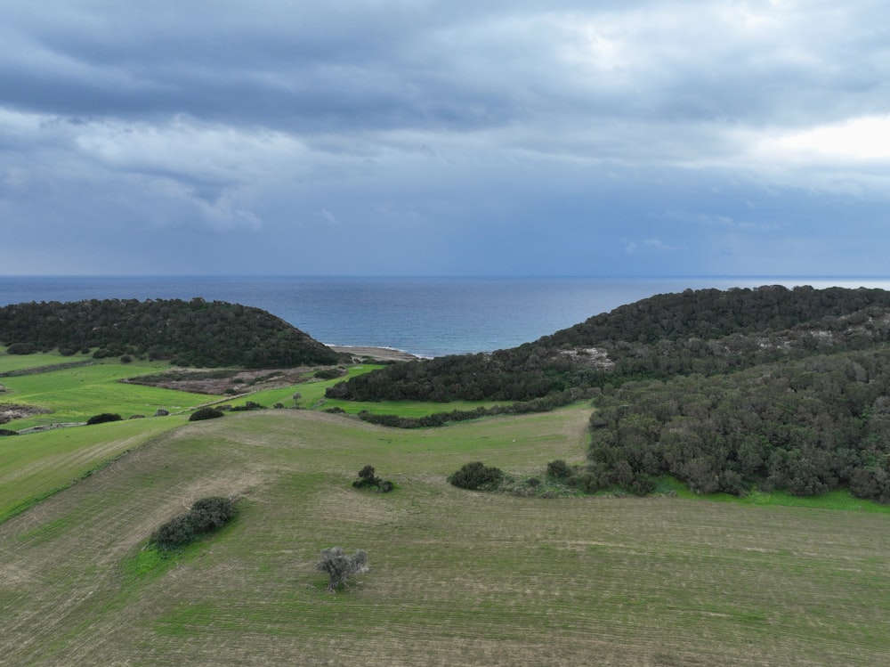 an aerial view of a grassy field with a body of water in the distance