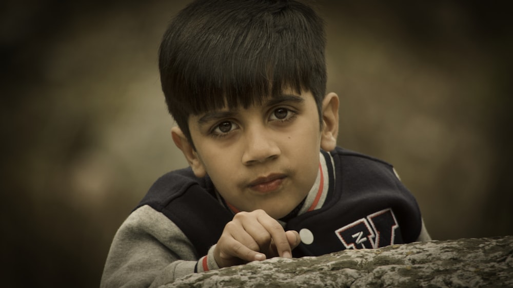 a young boy is leaning on a rock