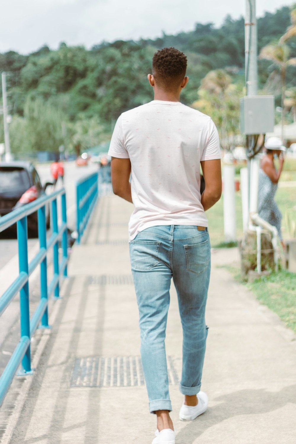 a man walking down a sidewalk next to a blue fence