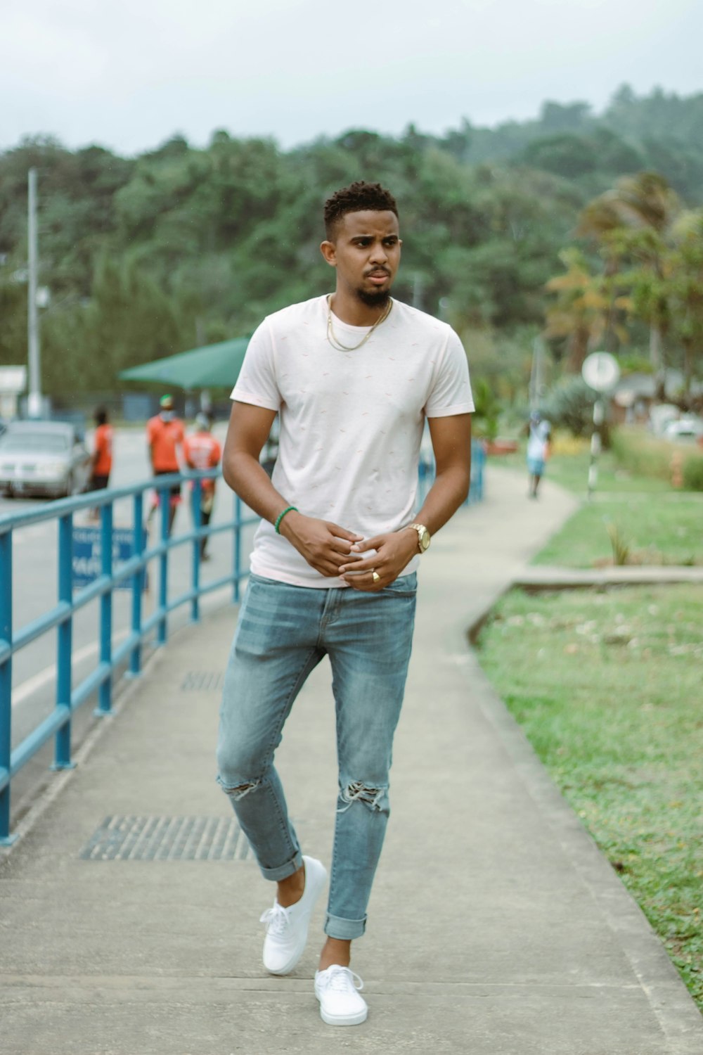 a man in white shirt and jeans walking down a sidewalk