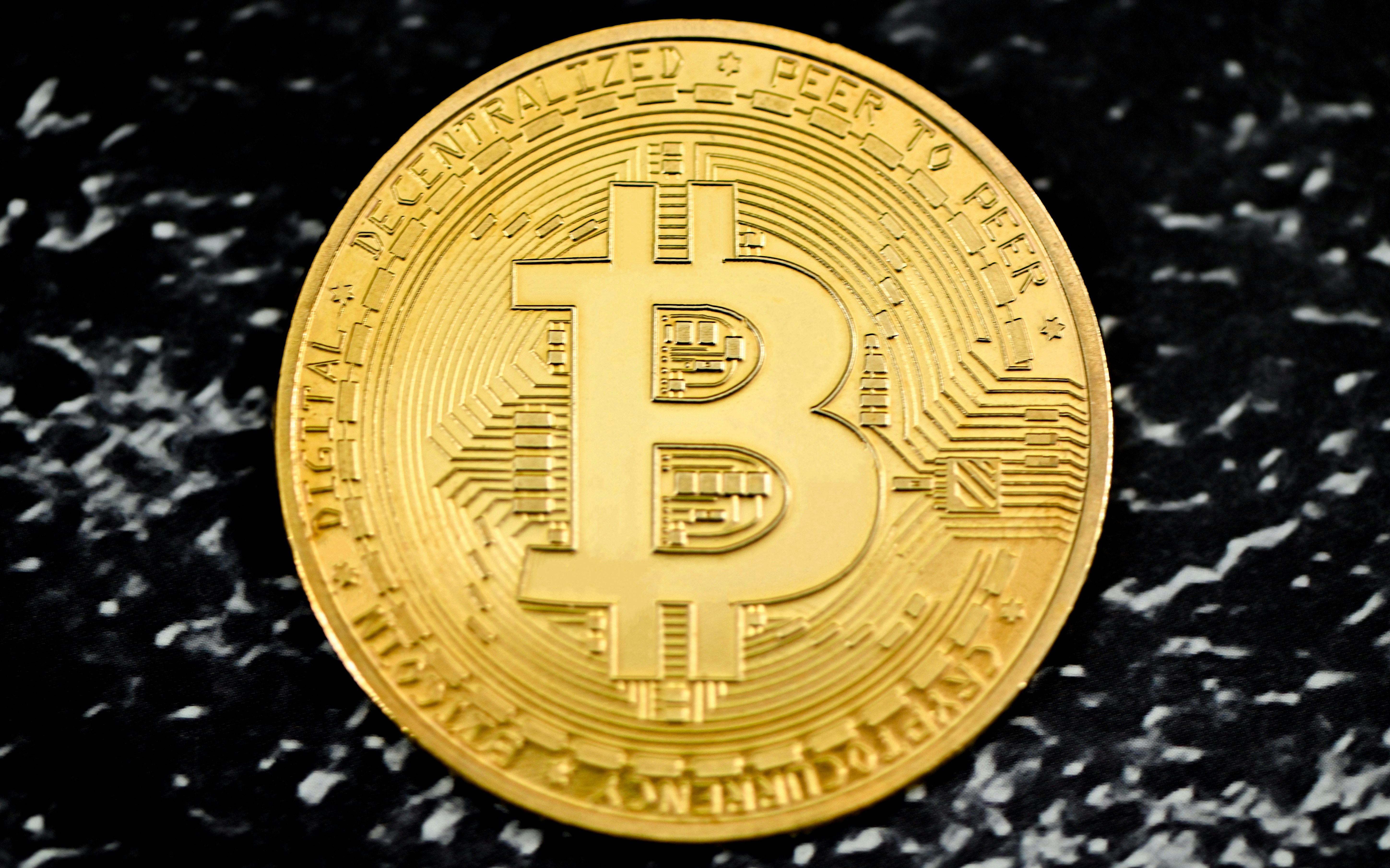 A gold Bitcoin on a black marble background