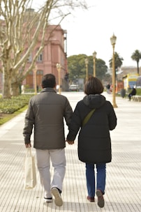 a man and woman walking down a sidewalk holding hands