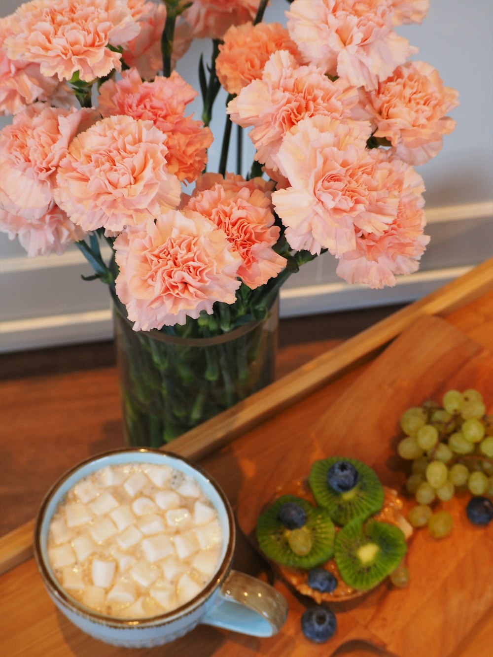 a vase of pink carnations next to a cup of hot chocolate