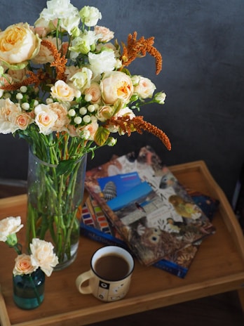 Fresh flowers arranged in a simple glass vase alongside a stack of art books on a light wood table.