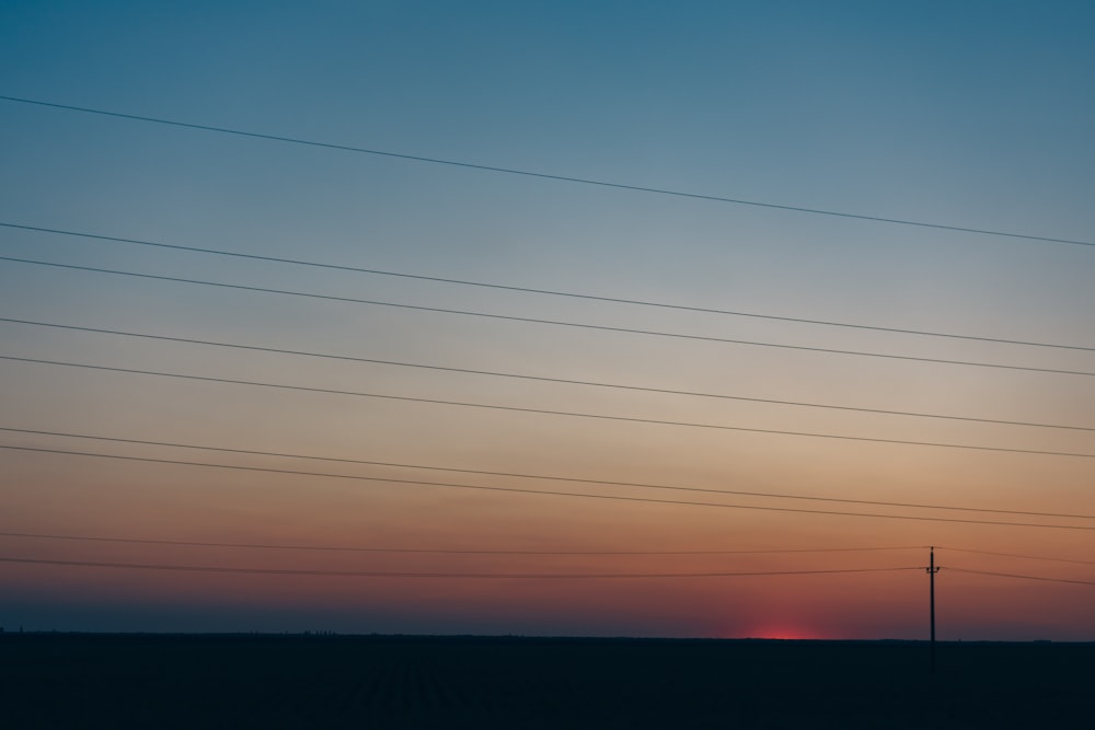 the sun is setting over a field with power lines