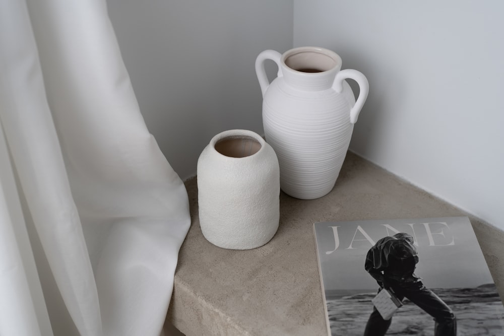 two white vases sitting on a table next to a magazine