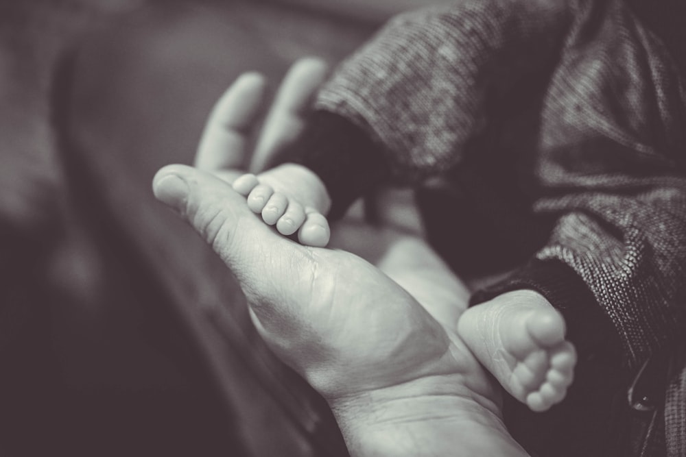 a black and white photo of a person holding a baby's foot