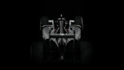 A sleek and aerodynamic Formula 1 car viewed from the front against a dark background. The car's contours and design elements are accentuated by the lighting, highlighting its sophisticated features.